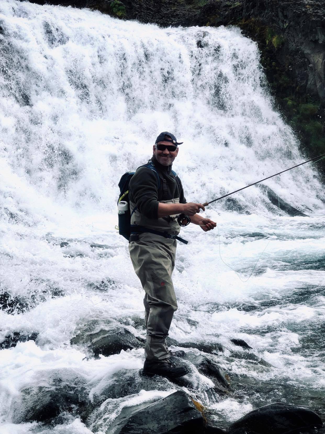 homme se tenant auprès d'une cascade lors d'un tour de pêche à la truite avec pêche islande.