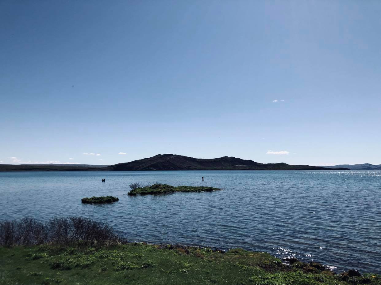 Trois Pêcheurs immergés dans le lac de Thingvallavatn en Islande, avec une montagne et le ciel bleu en arrière plan.