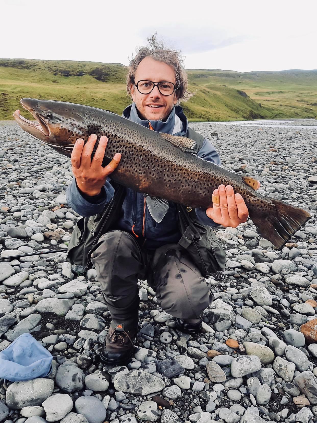 pêcheur accroupi tenant une grande truite de mer en Islande